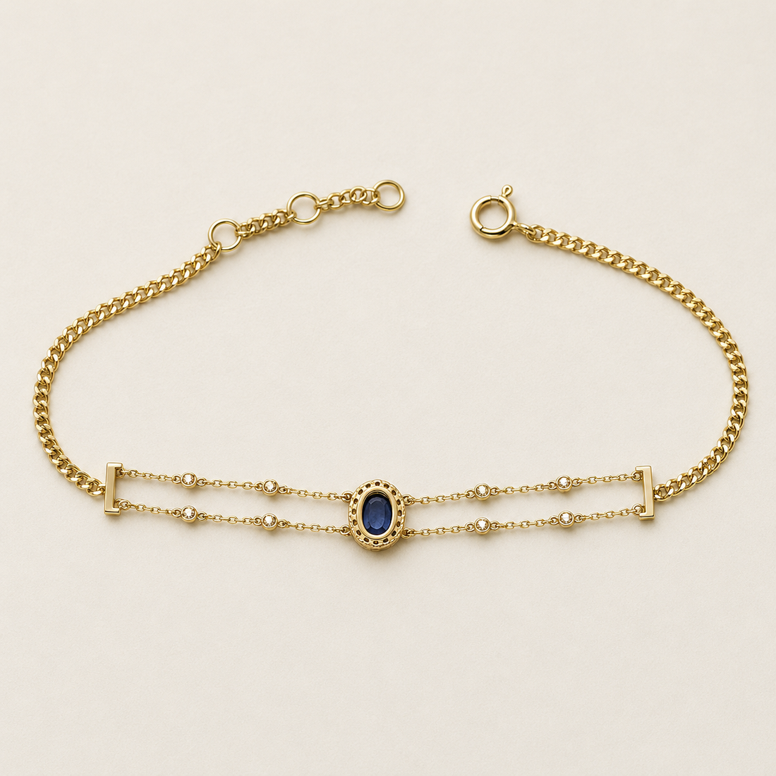 A gold chain bracelet featuring a central oval blue gemstone surrounded by a beaded gold border, with double parallel chains and small bead accents.