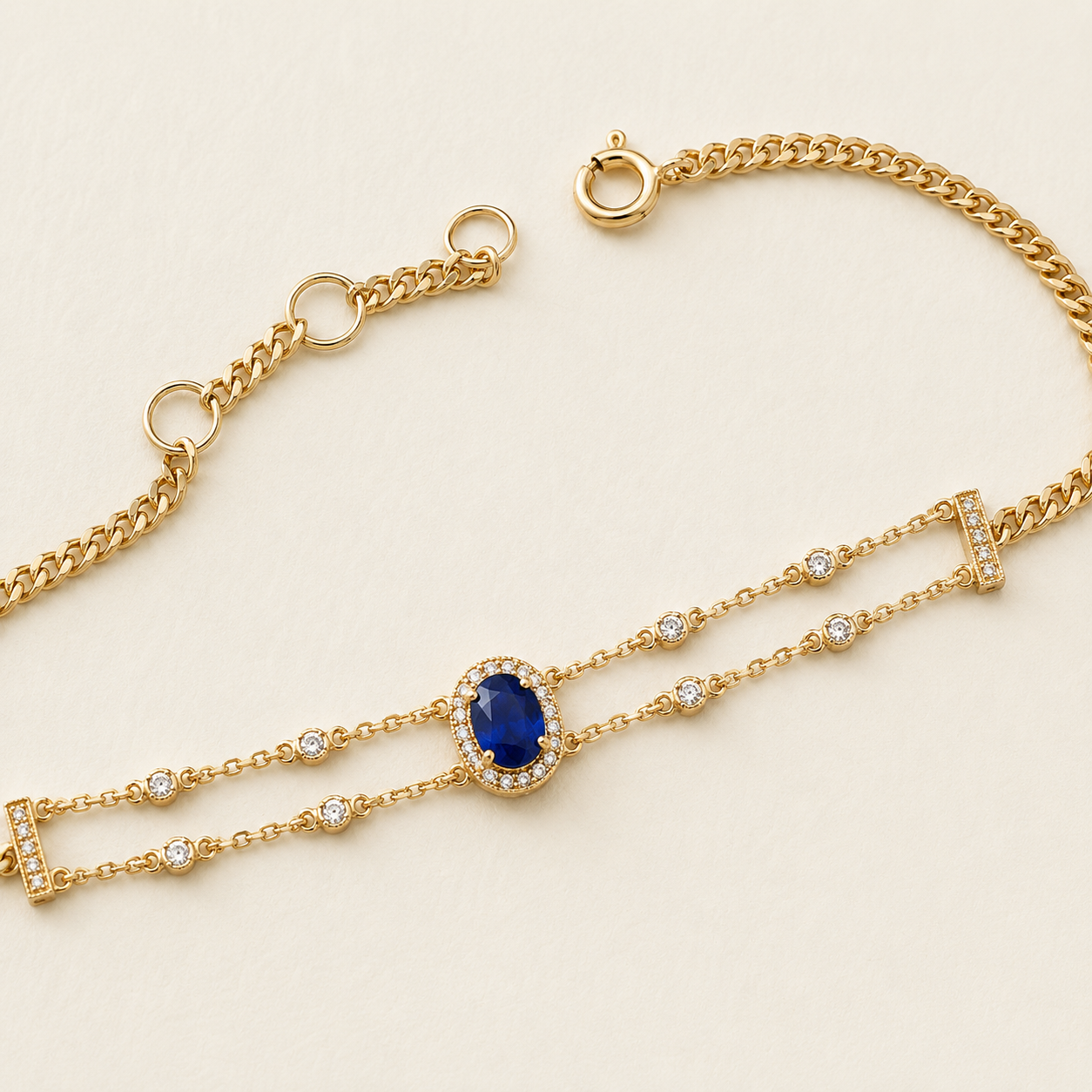 A gold chain bracelet featuring a central oval-cut blue sapphire surrounded by small clear stones, with additional clear stones set along the chain, displayed on a light cream background.