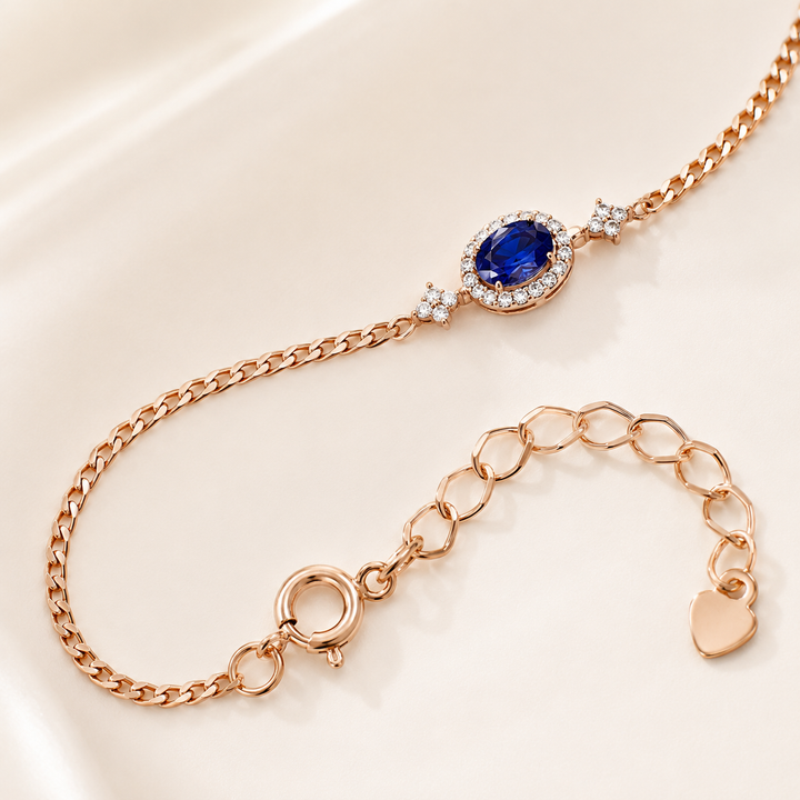 Rose gold chain bracelet featuring an oval blue sapphire center stone surrounded by small clear stones, with star accents and an adjustable link chain extender.