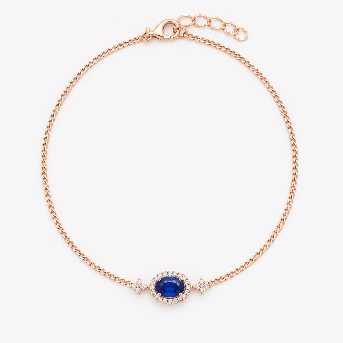 A delicate rose gold chain bracelet with an oval blue sapphire center stone surrounded by small clear accent stones, shown on a plain white background.