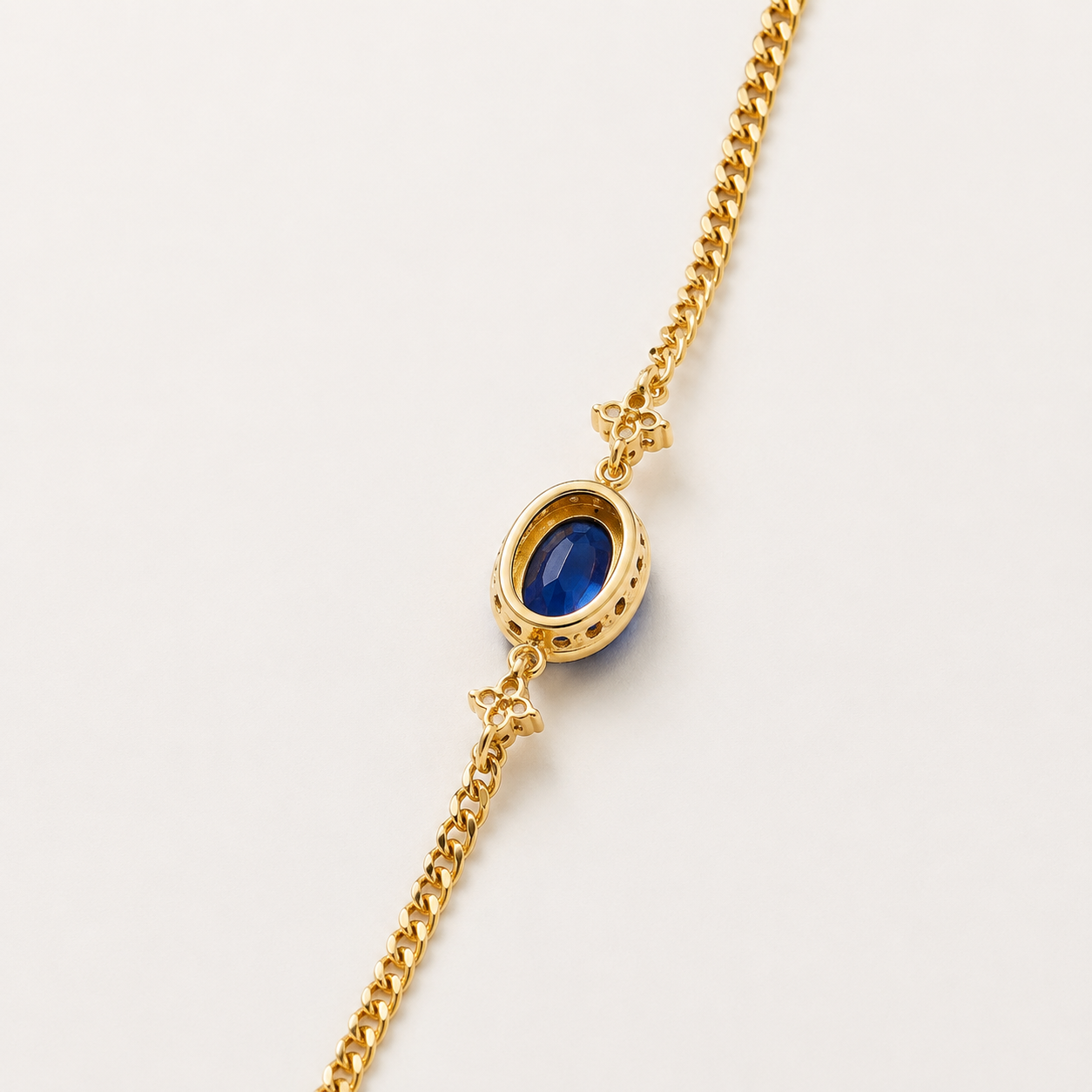 A gold chain bracelet featuring an oval bezel-set deep blue gemstone, photographed on a clean, light off-white background.
