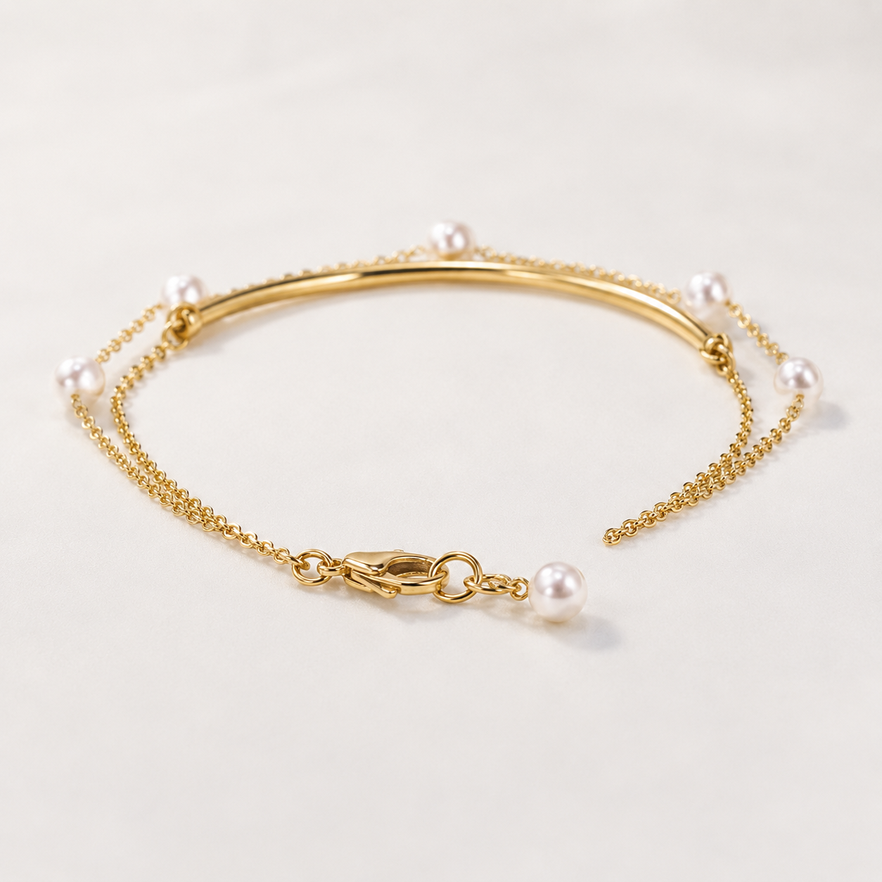 A delicate gold chain bracelet with small white pearls spaced along the chain and a lobster clasp closure, photographed on a clean off-white background.