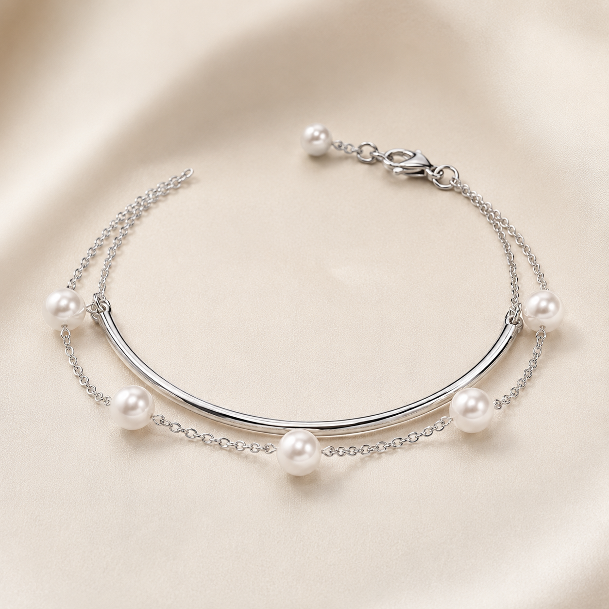 A silver-toned double-strand bracelet featuring a curved bar centerpiece and five white faux pearls spaced along the chain, displayed on a soft beige satin background.