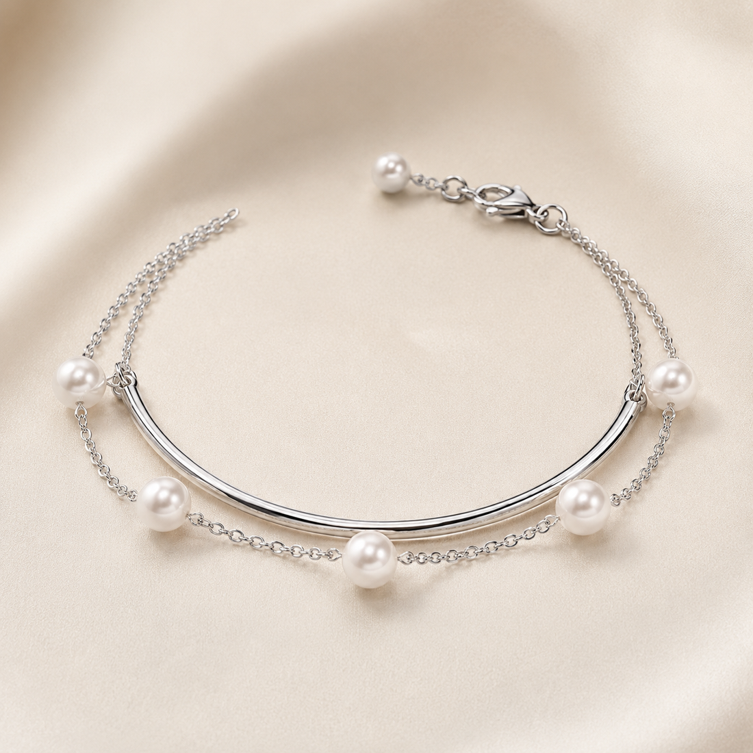 A silver-toned double-strand bracelet featuring a curved bar centerpiece and five white faux pearls spaced along the chain, displayed on a soft beige satin background.