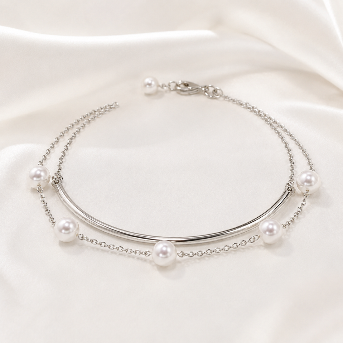 A silver-toned double-layered necklace featuring a curved bar and delicate chain links adorned with white freshwater pearls, displayed on a draped white satin fabric.