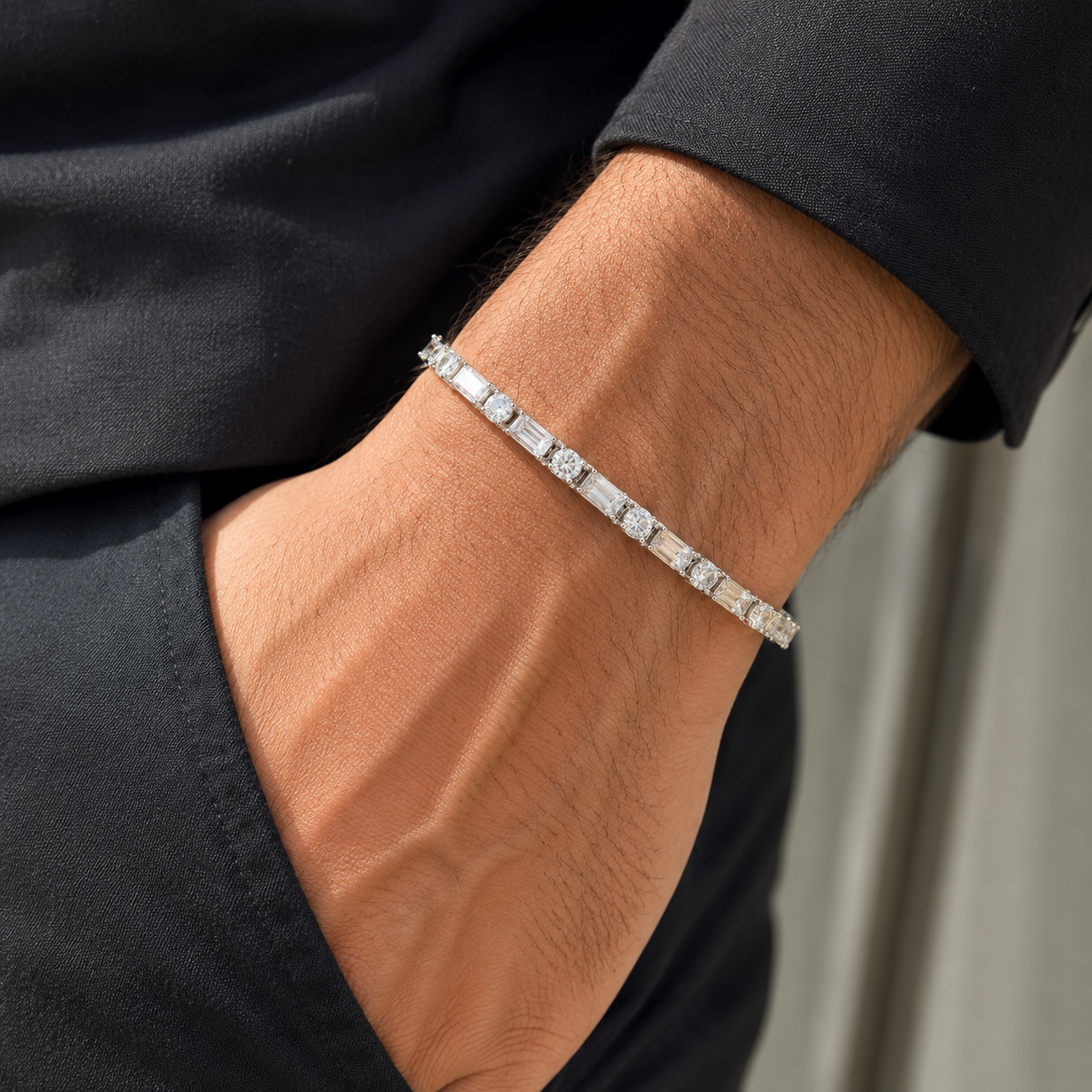 A close-up of a man's wrist wearing a silver tennis bracelet with baguette and round-cut stones, paired with a black shirt.