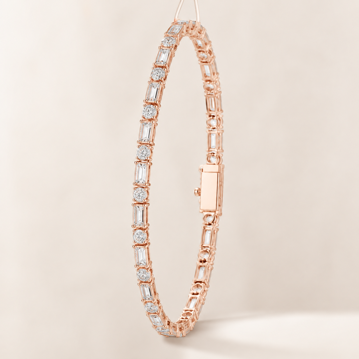 A rose gold tennis bracelet with baguette-cut clear stones, shown hanging against a warm beige background.