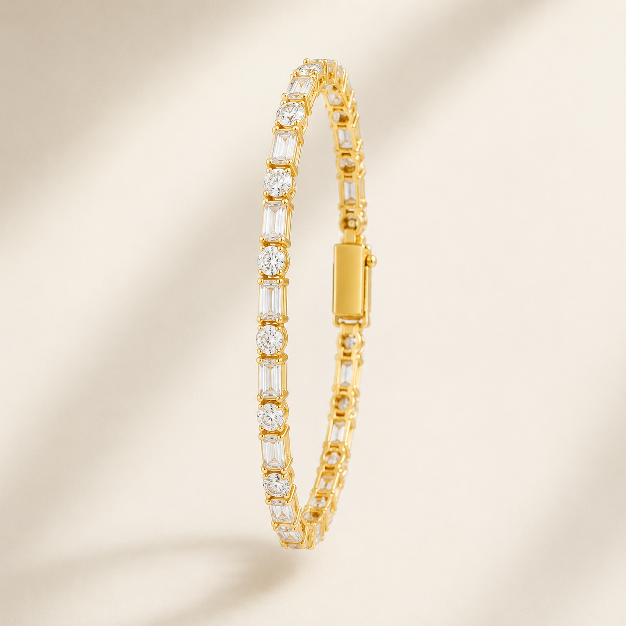 A gold tennis bracelet with baguette and round-cut clear stones, shown standing vertically against a warm beige background with soft shadows.