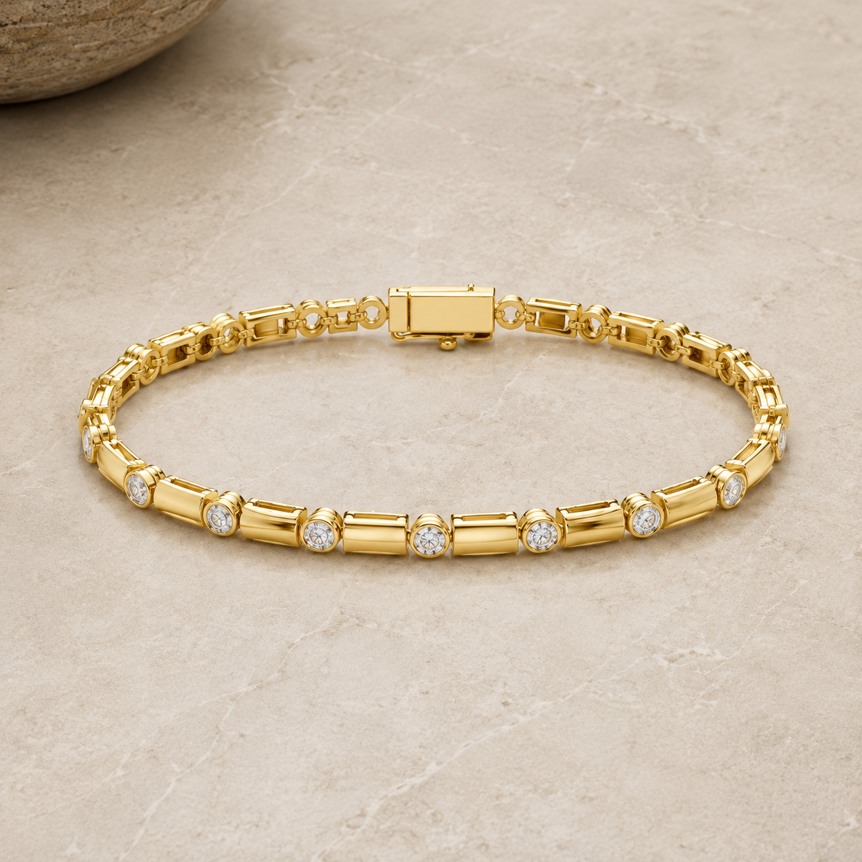 A gold tennis bracelet with round-cut clear stones set along the front, displayed on a light beige stone surface.