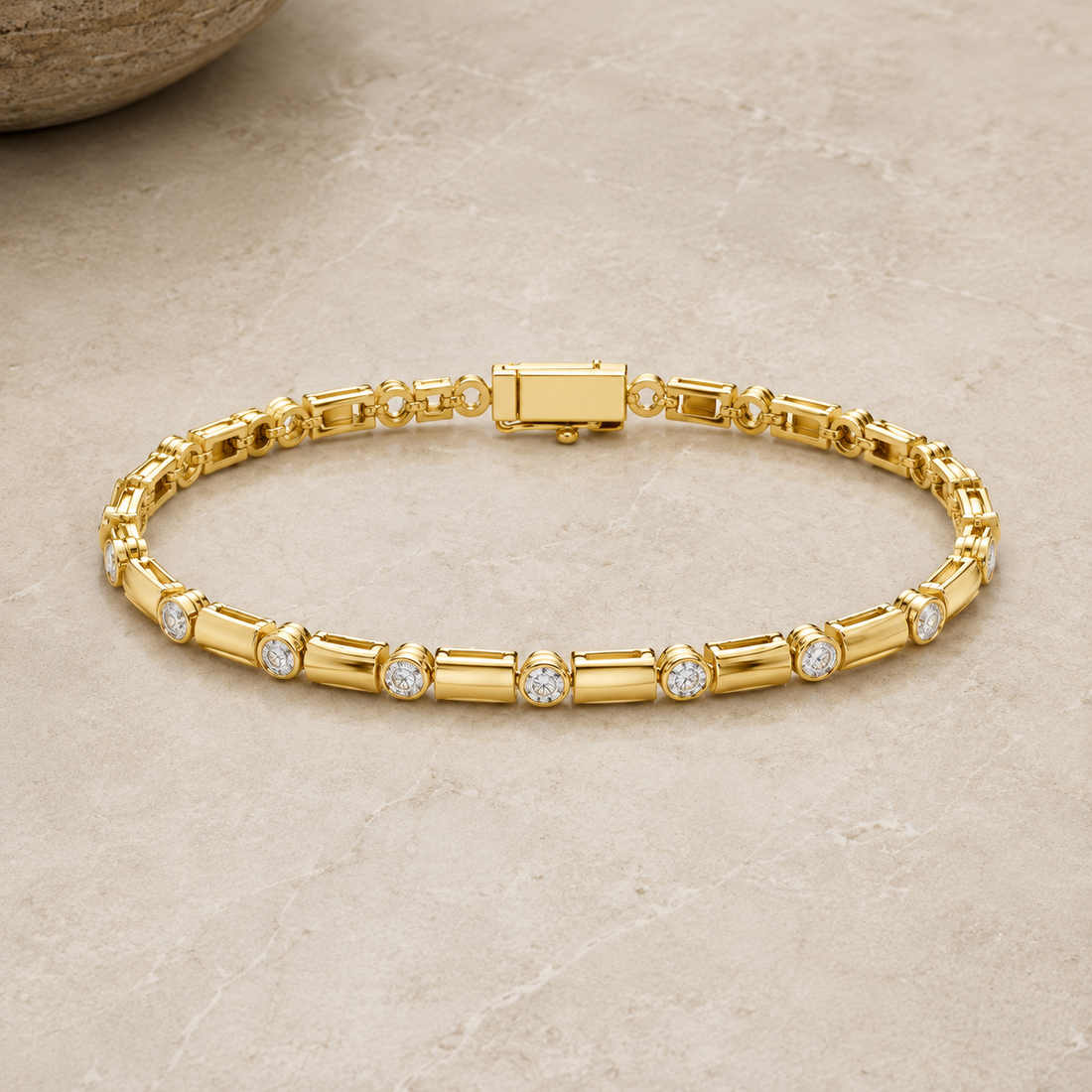 A gold tennis bracelet with round-cut clear stones set along the front, displayed on a light beige stone surface.