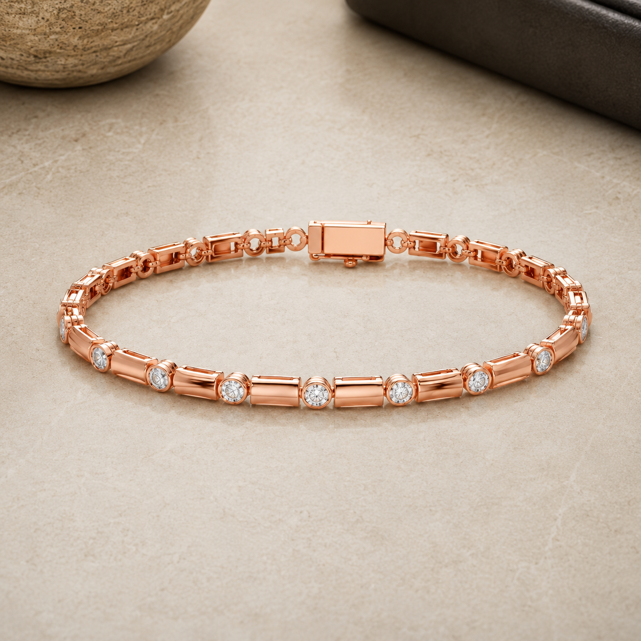 A rose gold tennis bracelet with baguette and round-cut stone links, displayed on a neutral beige stone surface.
