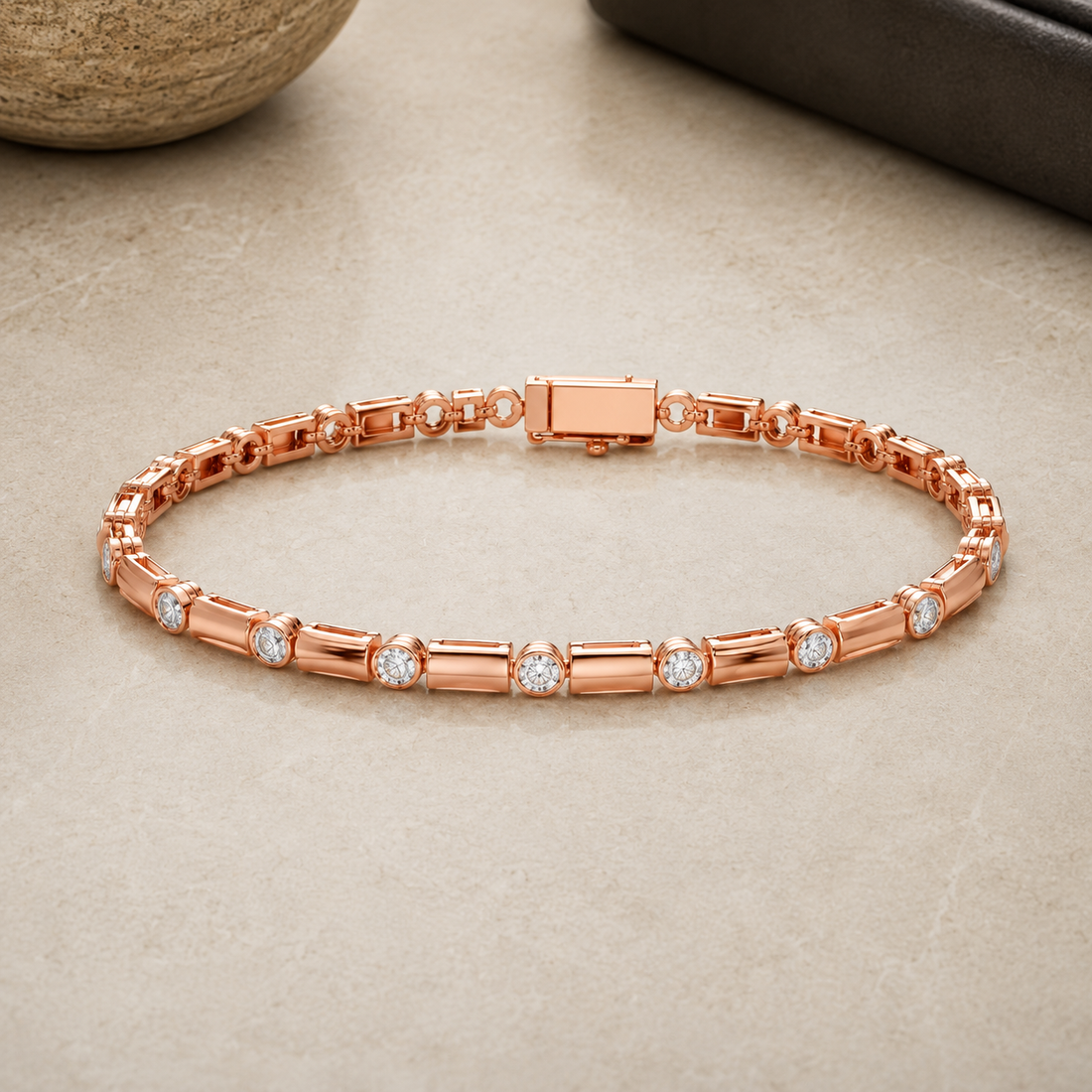 A rose gold tennis bracelet with baguette and round-cut stone links, displayed on a neutral beige stone surface.