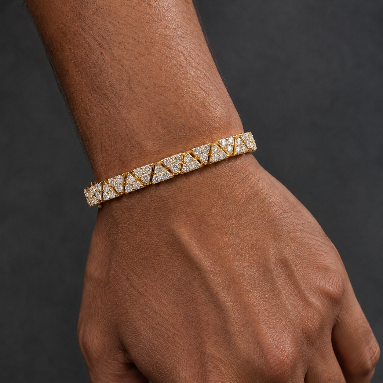 A close-up of a person's wrist and hand wearing a gold tennis bracelet set with clear gemstones, set against a dark gray background.