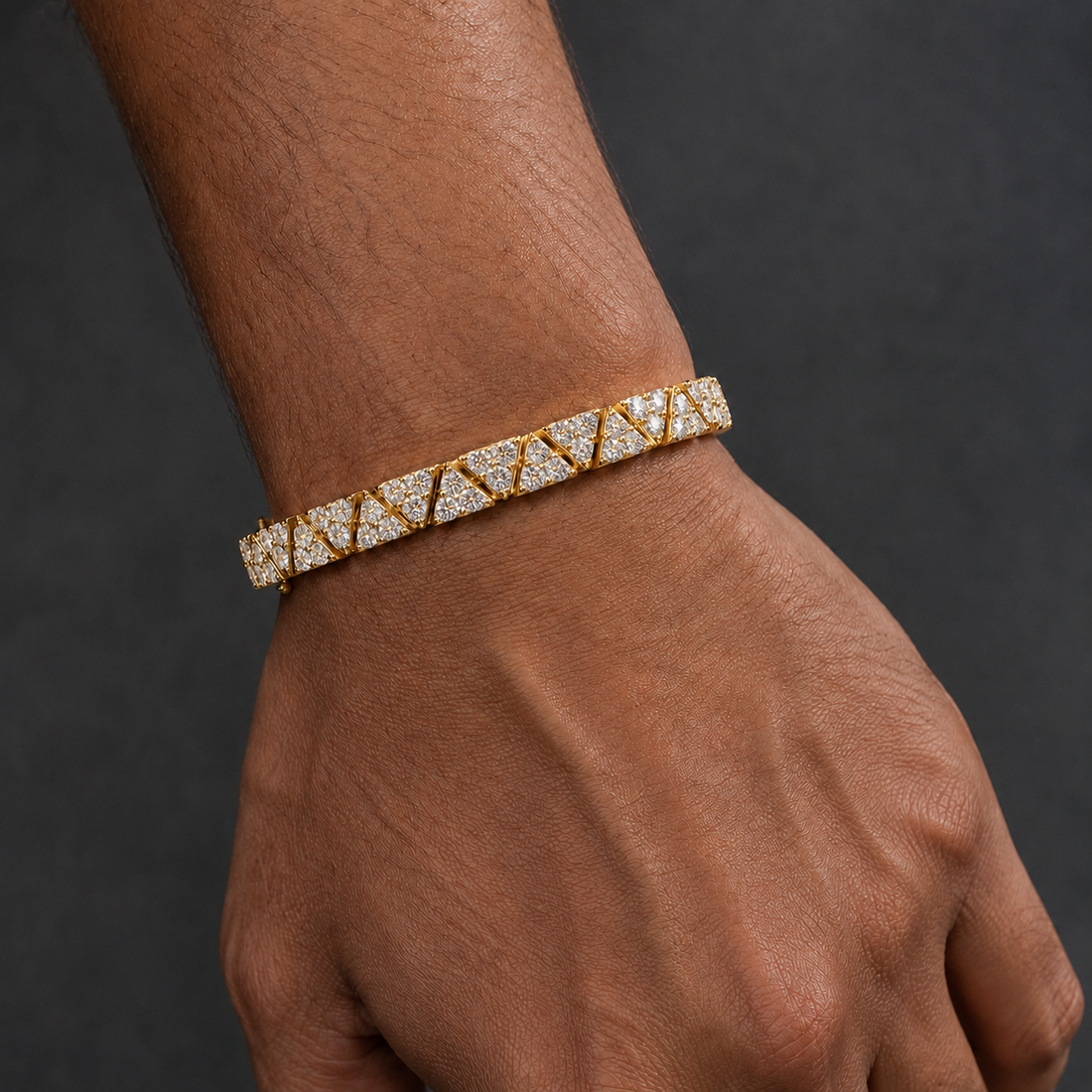 A close-up of a person's wrist and hand wearing a gold tennis bracelet set with clear gemstones, set against a dark gray background.