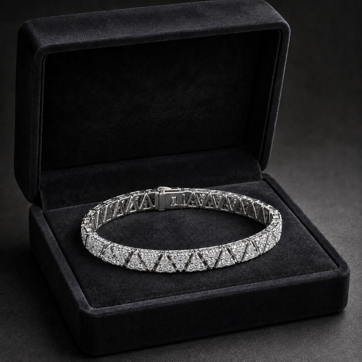 A silver-toned tennis bracelet paved with small clear stones, displayed inside an open black velvet jewelry box on a dark background.