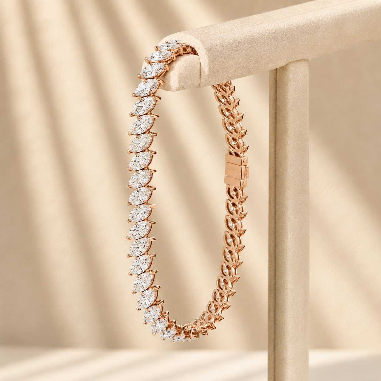 A rose gold tennis bracelet with marquise-cut clear stones, displayed on a beige jewelry stand against a softly lit beige fabric background.