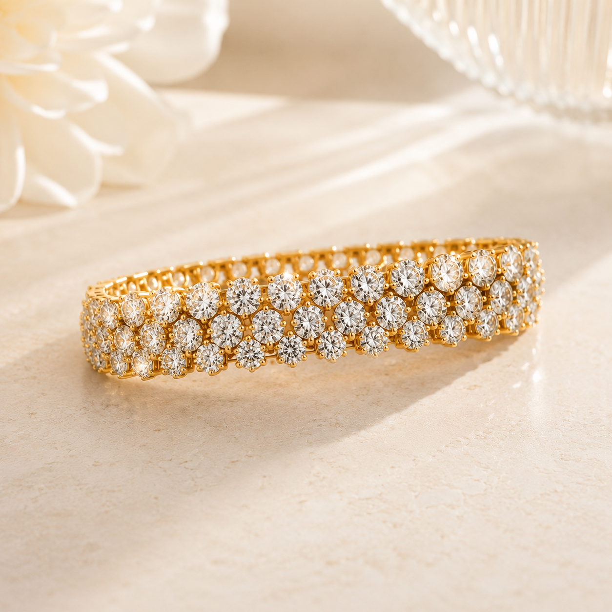 A gold tennis bracelet adorned with rows of sparkling clear gemstones, displayed on a light beige surface with soft-focus white floral elements in the background.