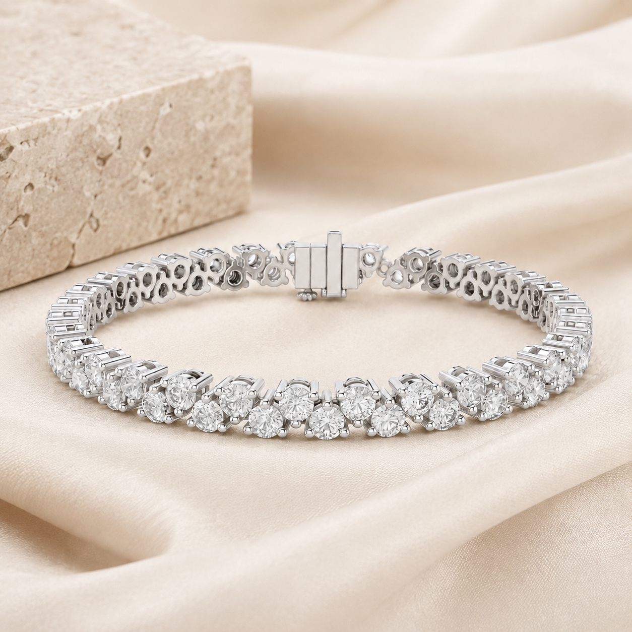 A silver tennis bracelet with round-cut clear stones, displayed on draped beige satin fabric next to a textured stone block.