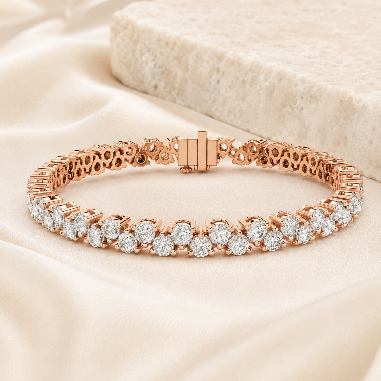 A rose gold tennis bracelet with round-cut clear stones, displayed on draped cream satin fabric with a textured stone prop in the background.