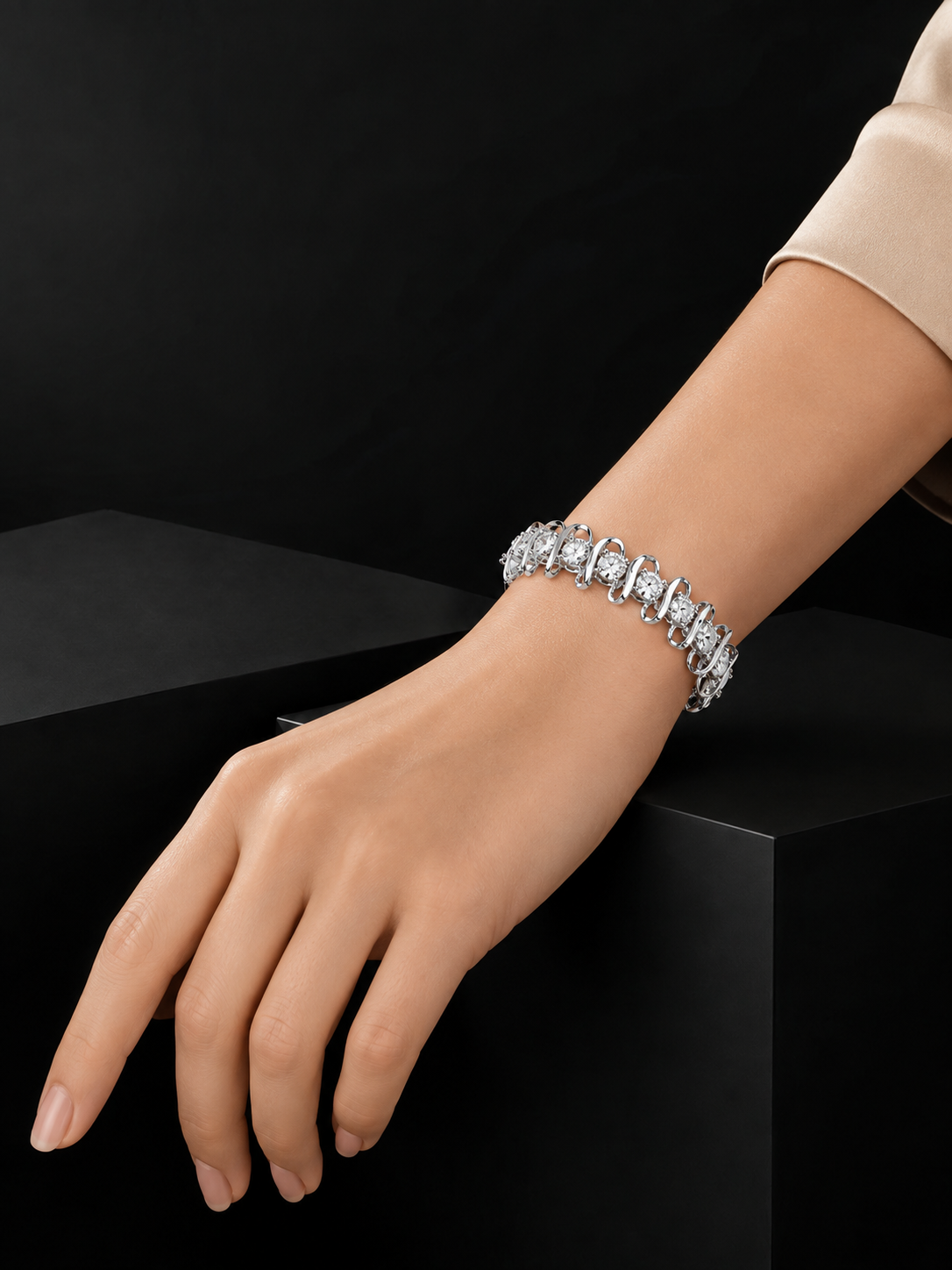 A close-up of a woman's wrist and hand wearing a sparkling diamond tennis bracelet, posed against a dark black background with a black display block.
