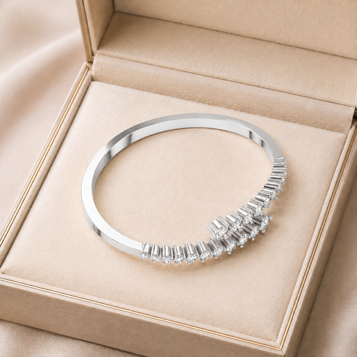 A polished silver-toned bangle bracelet with a curved row of clear baguette-cut stones, displayed inside an open beige jewelry box.