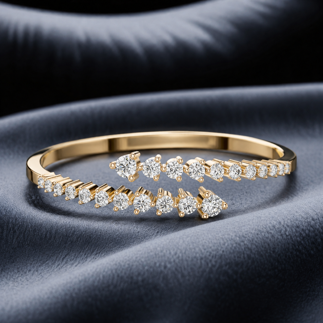 A gold wrap-style bangle bracelet adorned with multiple rows of sparkling round-cut diamonds, displayed on a draped dark navy blue fabric background.