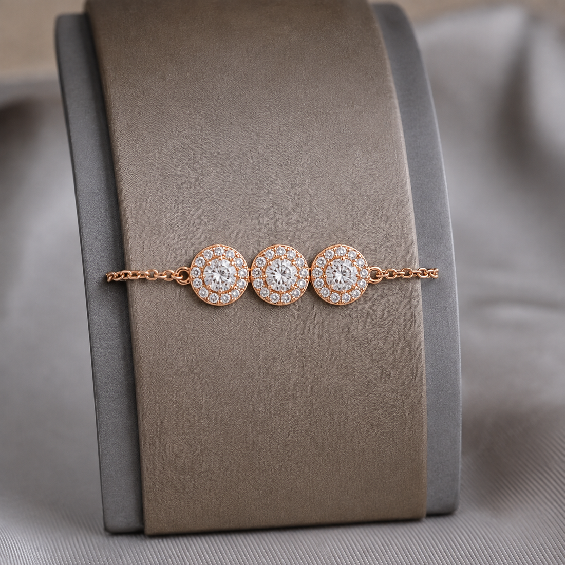 A rose gold bracelet with three circular diamond clusters, displayed on a gray velvet jewelry stand.