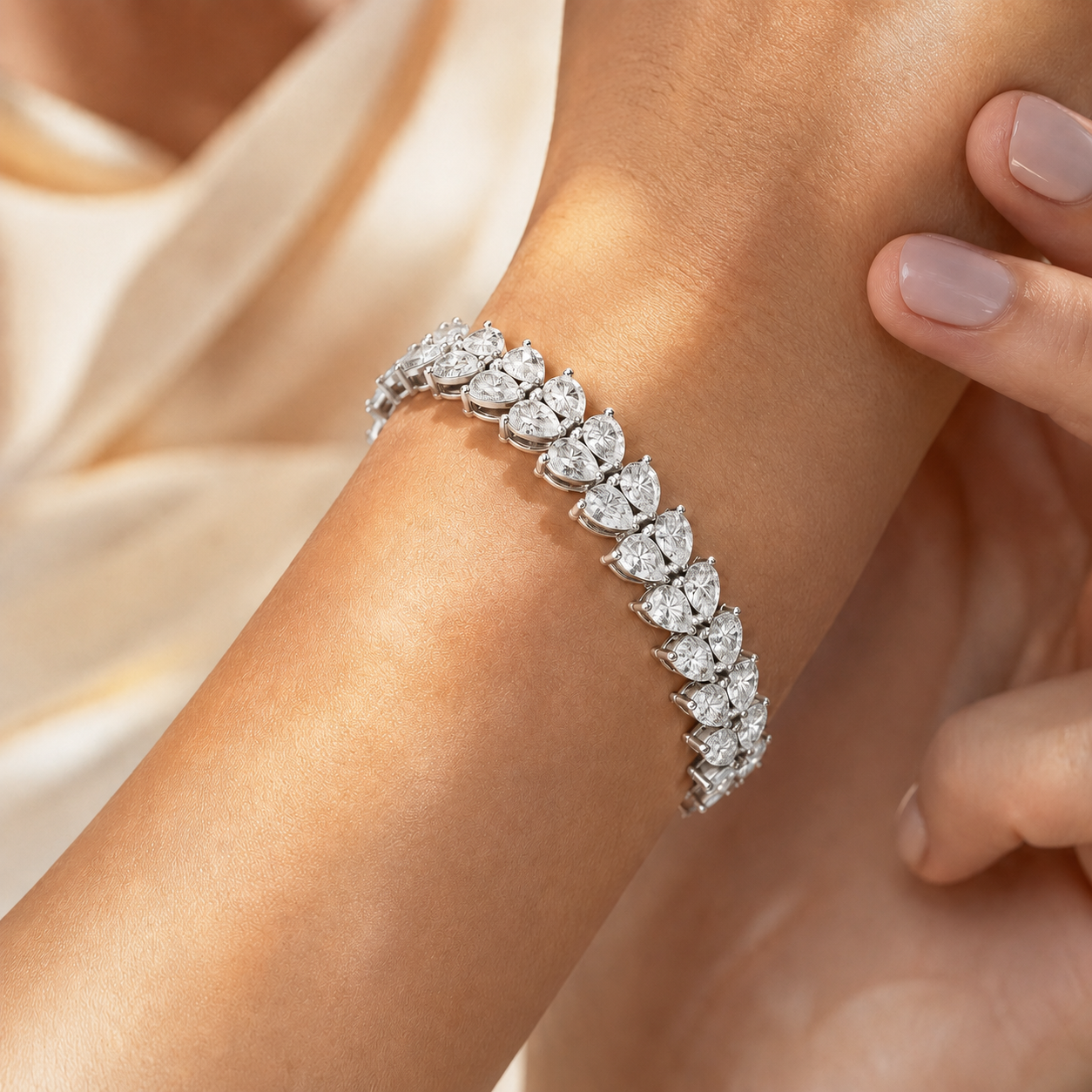 A close-up of a diamond bracelet with pear-cut stones set in a silver-toned metal, worn on a woman's wrist with her fingers gently touching the side.