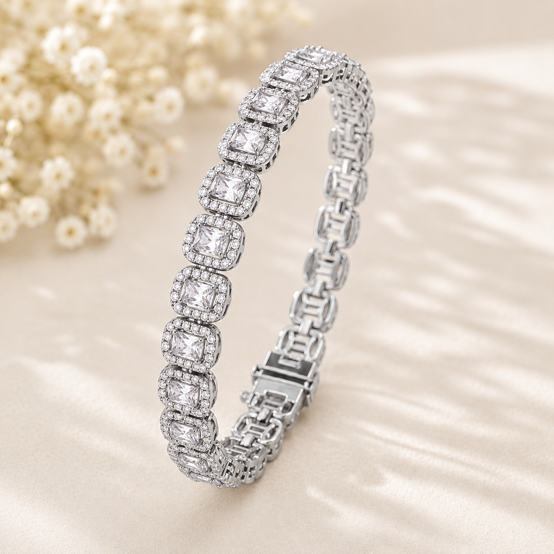A silver tennis bracelet with cushion-cut and round diamonds, displayed on a beige satin fabric with small white flowers in the background.