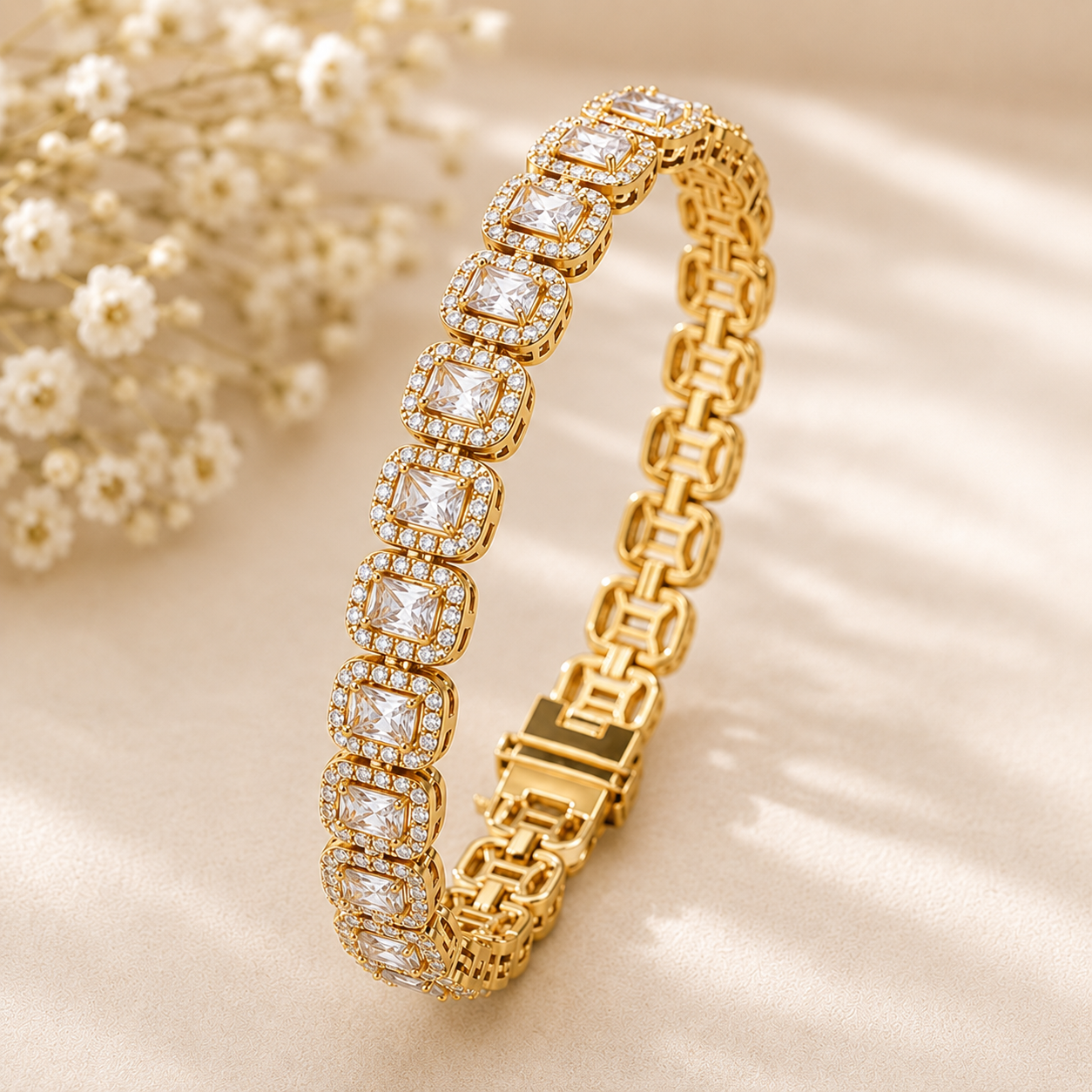 A gold tennis bracelet with square-cut clear gemstones, displayed on a soft beige satin fabric with small white flowers in the background.
