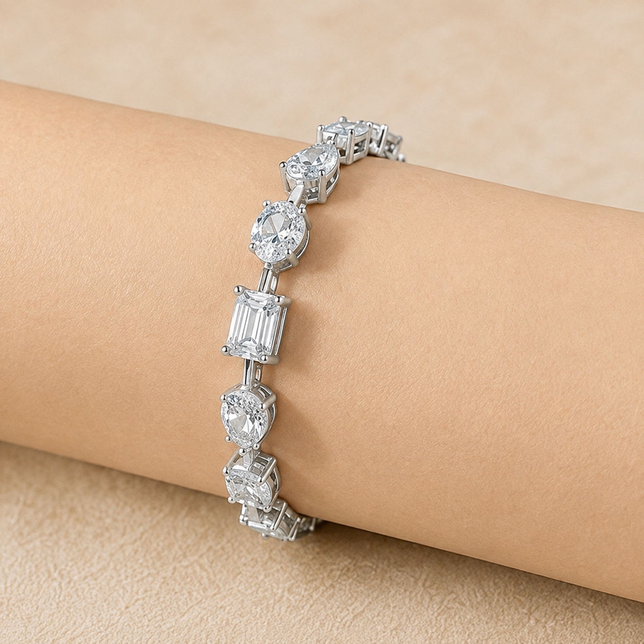 A silver-toned tennis bracelet with clear baguette and round-cut stones, shown worn on a person's wrist against a soft beige background.