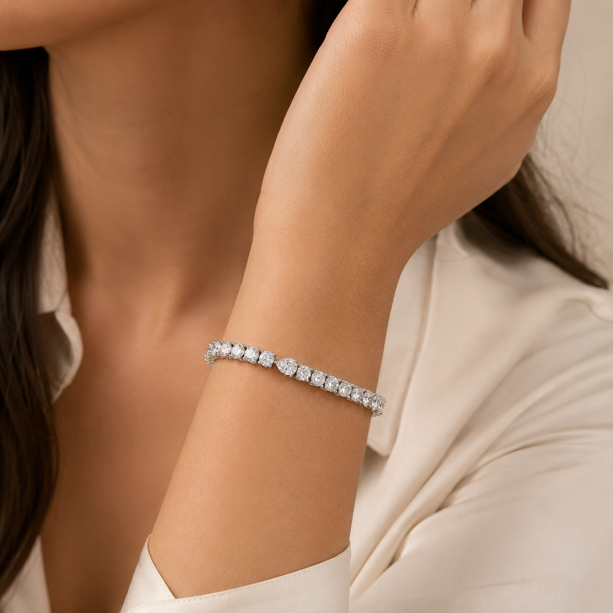 A close-up of a woman's wrist wearing a sparkling silver tennis bracelet with clear gemstones, paired with a cream-colored blouse.