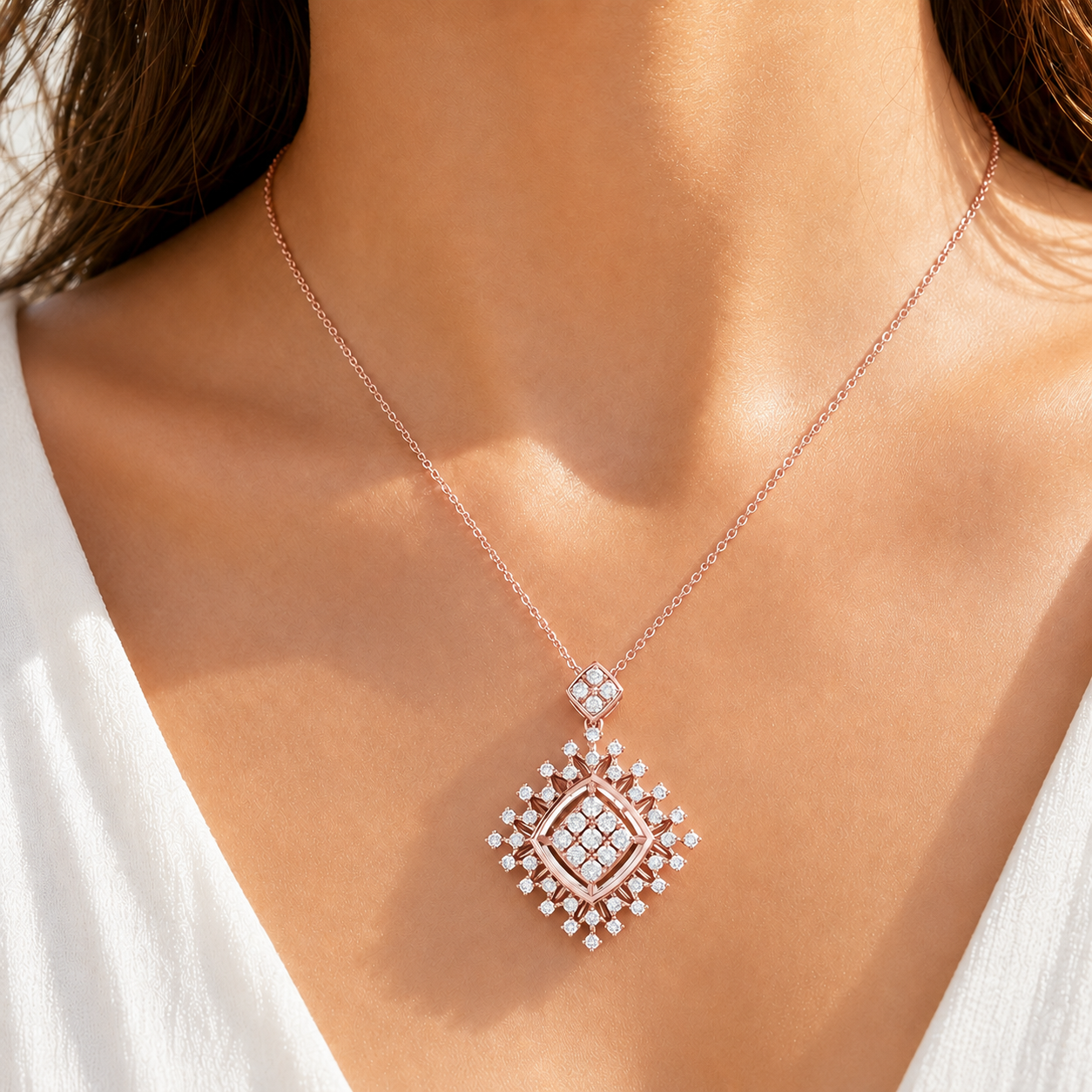 A close-up of a model wearing a delicate rose gold chain necklace with a geometric diamond-shaped pendant set with clear gemstones.