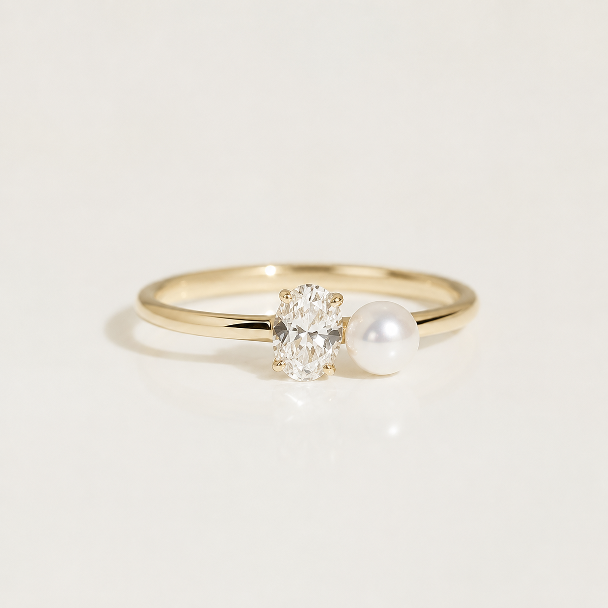 A gold ring featuring an oval-cut clear gemstone and a white pearl set side by side on a polished band, photographed on a clean white background.