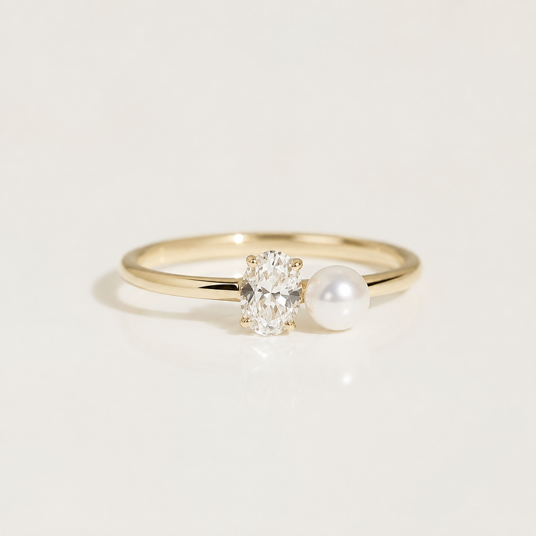 A gold ring featuring an oval-cut clear gemstone and a white pearl set side by side on a polished band, photographed on a clean white background.