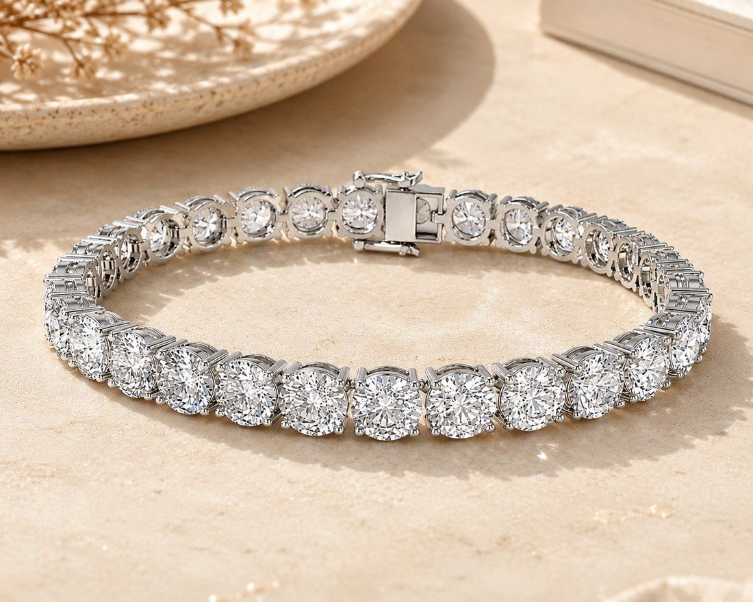 A silver tennis bracelet with round-cut clear stones, displayed on a light beige textured surface with a decorative plate in the background.