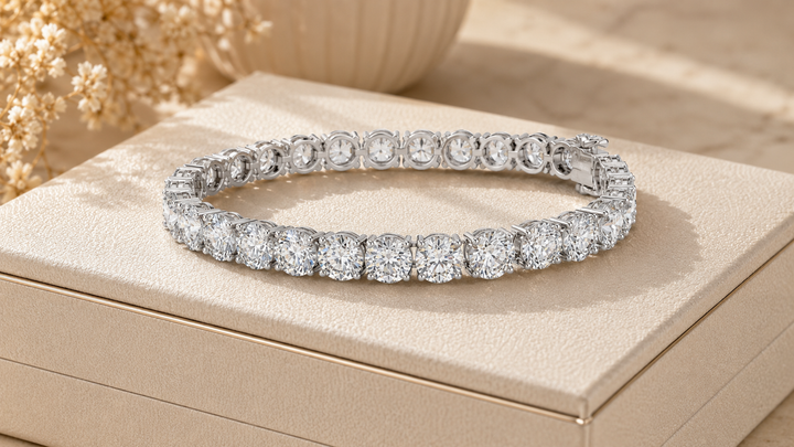 A silver tennis bracelet with round-cut clear stones, displayed on a beige jewelry box with dried floral decor in the background.