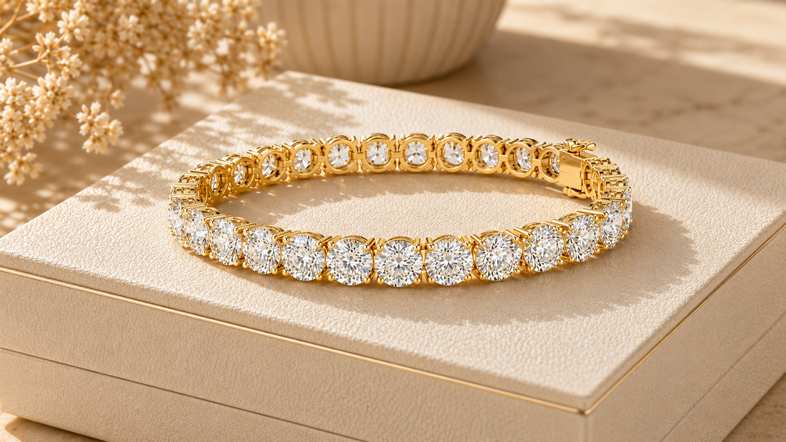 A gold tennis bracelet with round clear gemstones, displayed on a beige jewelry box with dried flowers in the background.