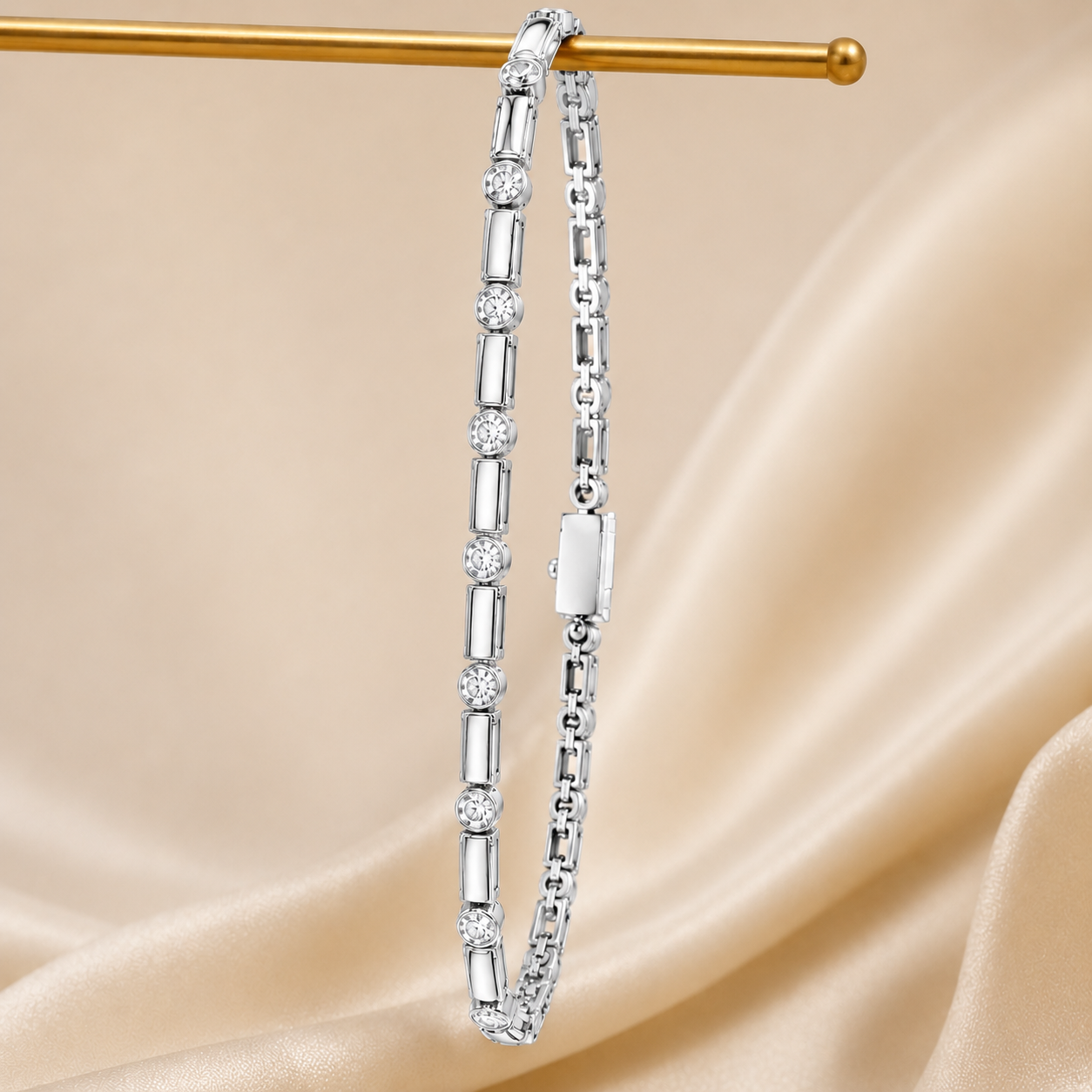 A silver tennis bracelet with alternating round and baguette-cut clear stones, hanging from a gold display rod against a draped beige satin background.