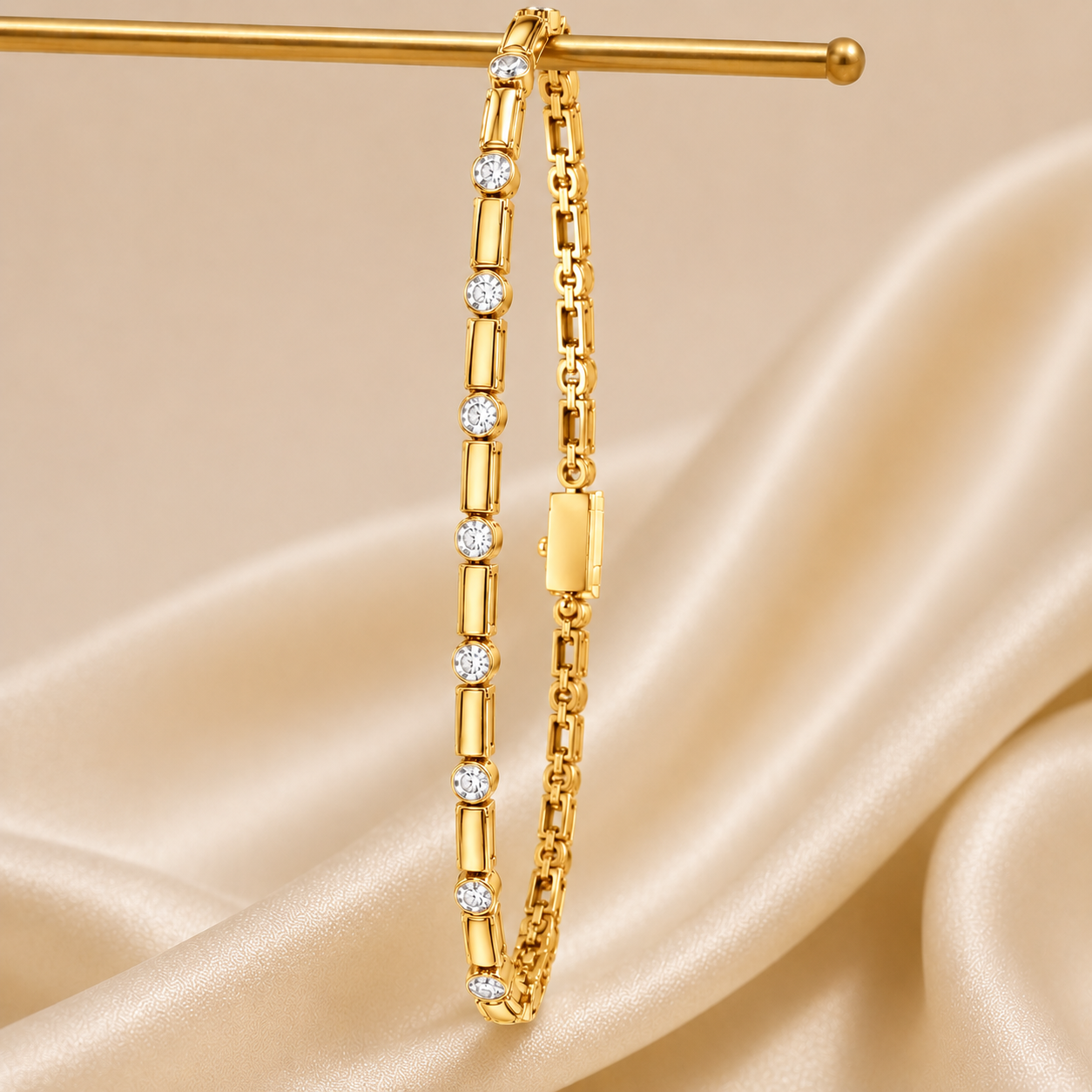 A gold tennis bracelet with round-cut clear stones, hanging from a gold display stand against a draped beige satin fabric background.