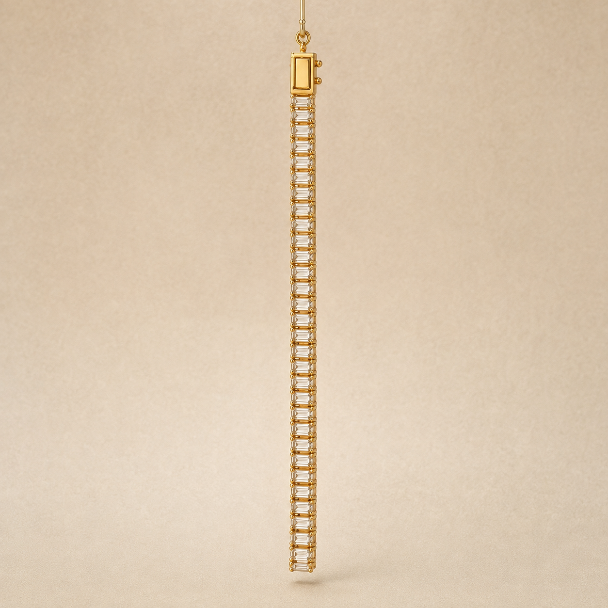 A single long drop bracelet in yellow gold, featuring a vertical row of clear rectangular baguette-cut stones, suspended against a textured beige background.