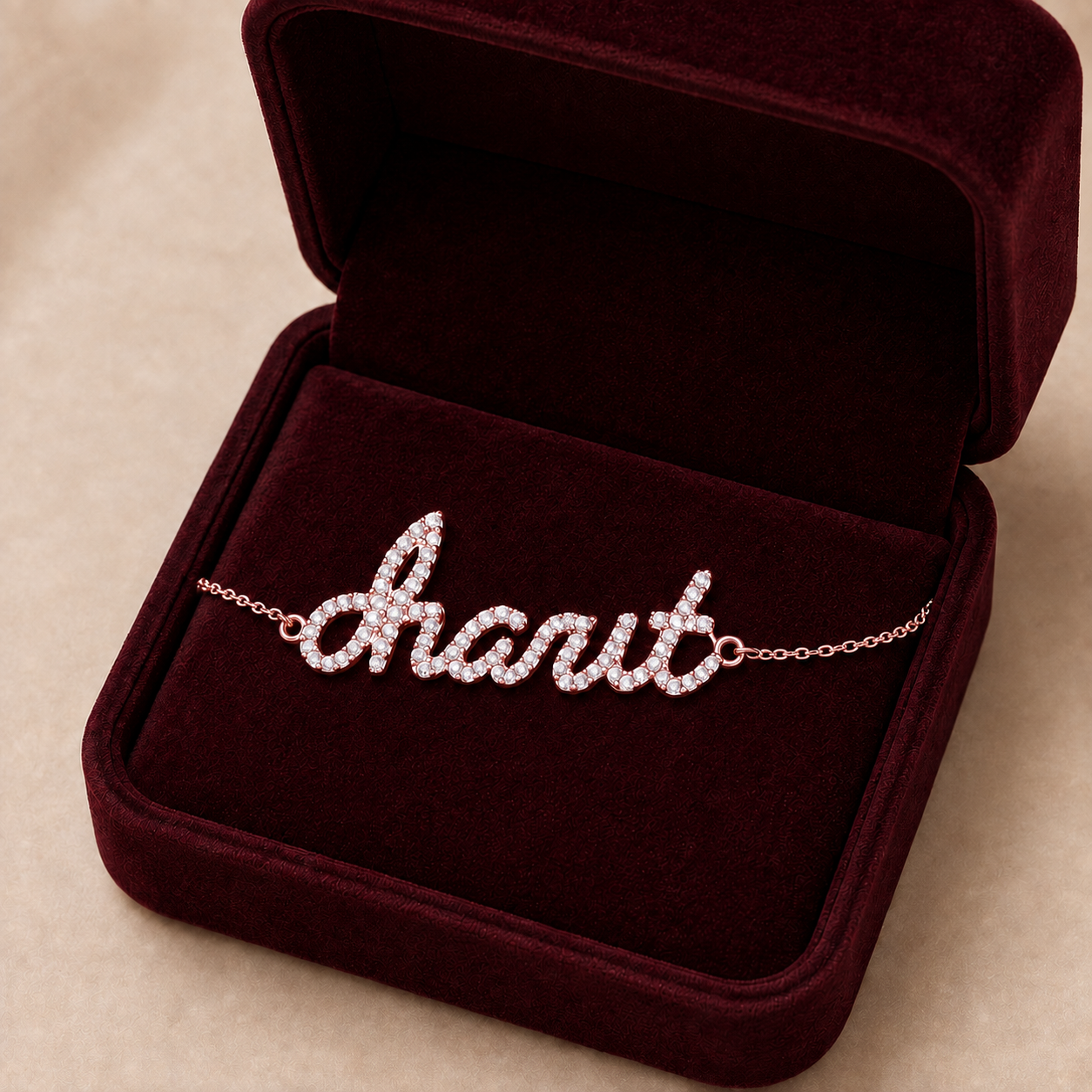A personalized name bracelet spelling charit  in sparkling script, displayed inside an open dark burgundy velvet jewelry box on a beige surface.