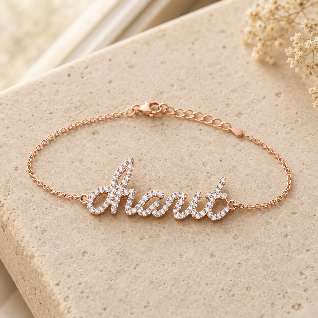 A rose gold script nameplate bracelet spelling charit  with clear pavé stones, displayed on a textured beige stone surface.