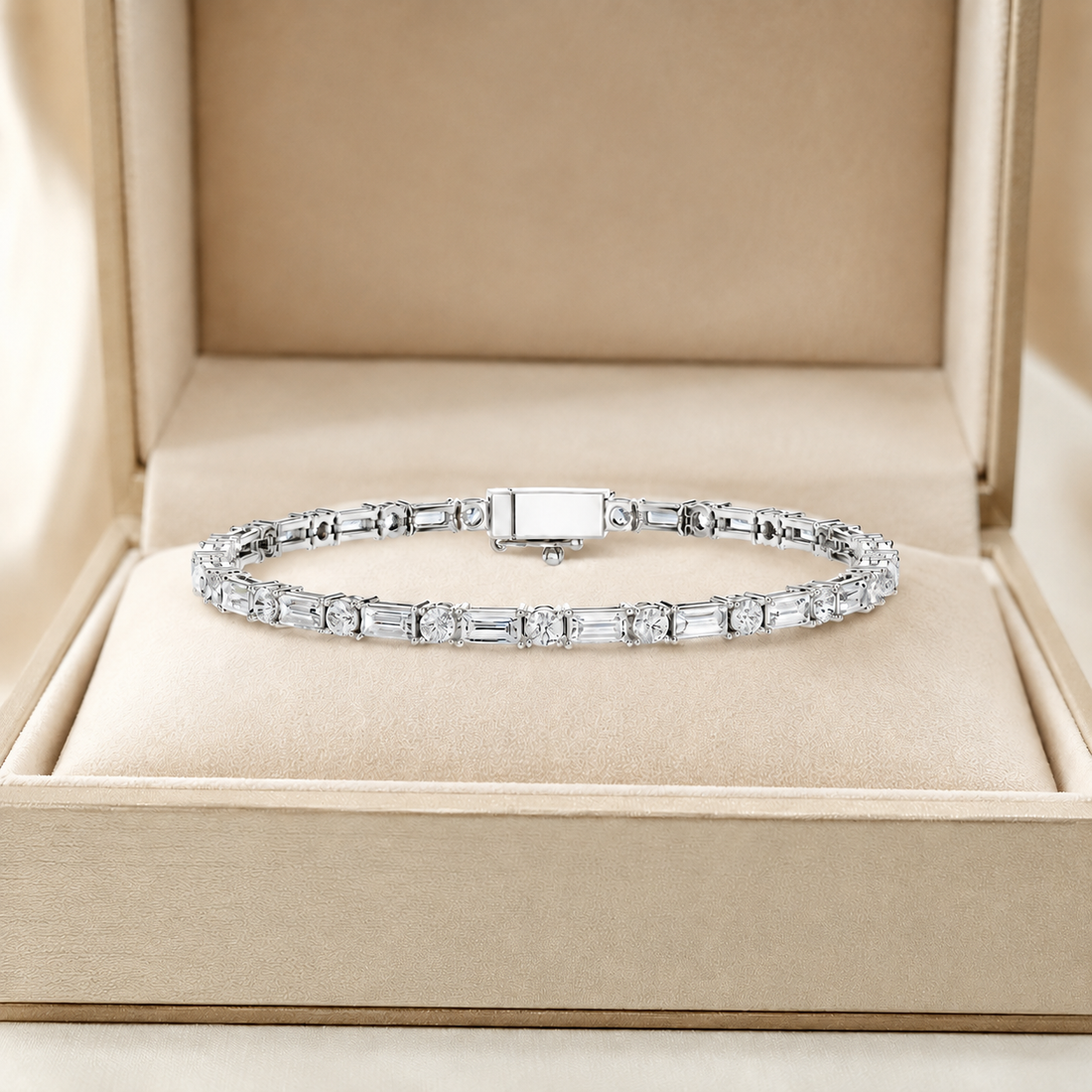 A silver tennis bracelet with baguette and round clear stones, displayed inside an open beige jewelry box.