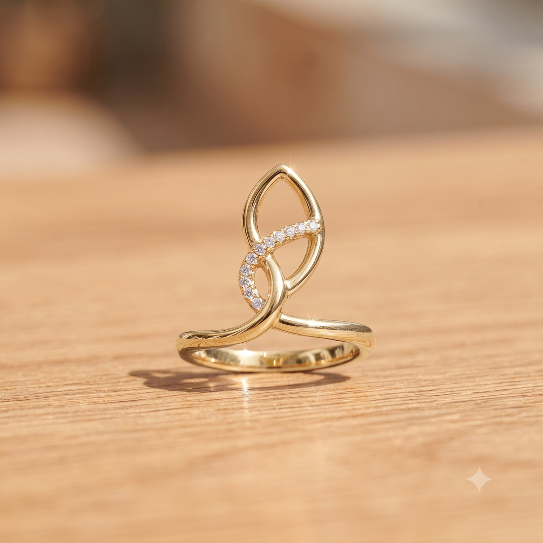 A gold ring with an abstract, flowing openwork design and a curved section set with small clear stones, resting on a light wooden surface.