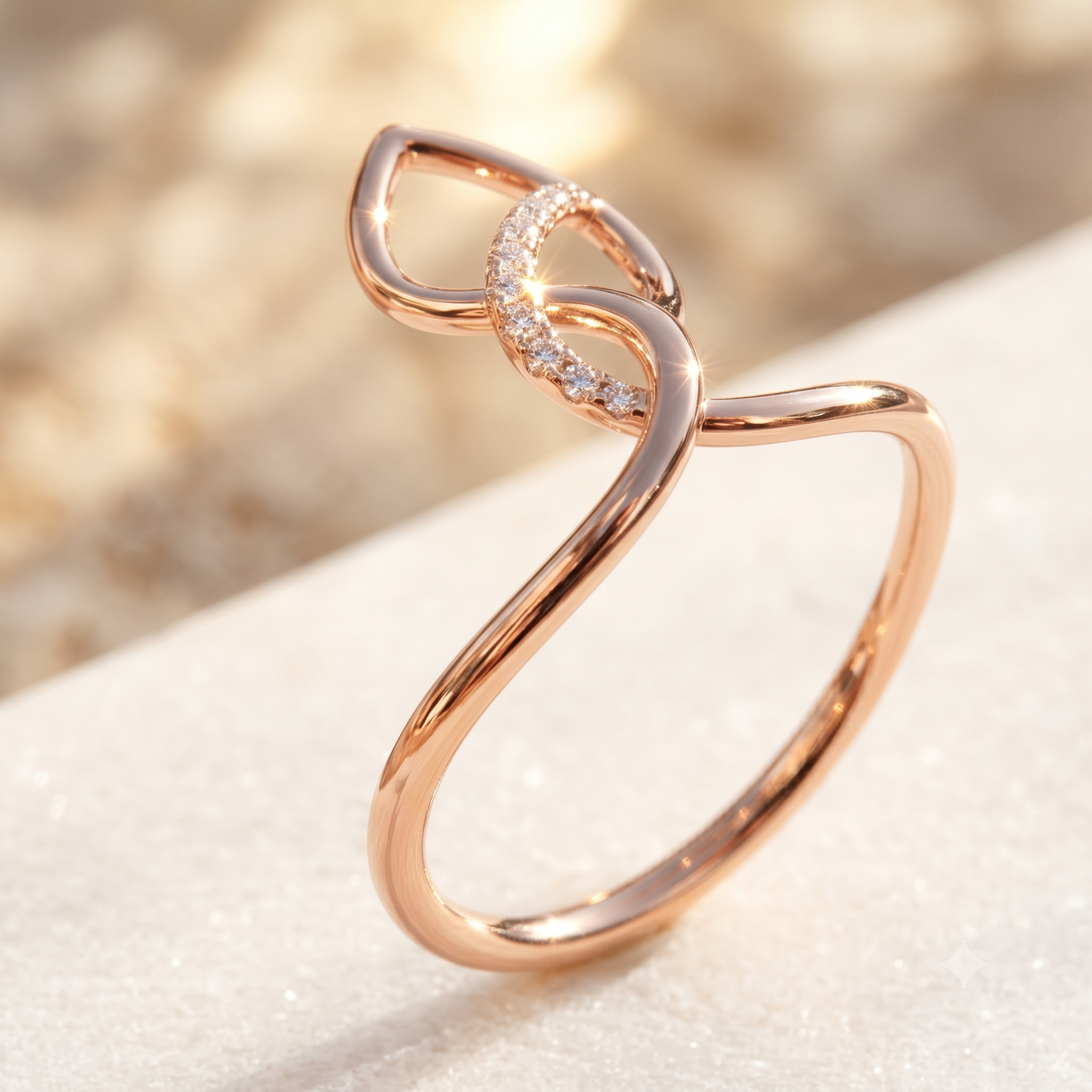 A rose gold ring with a sculptural, flowing openwork design and a small curved row of clear stones, displayed on a textured light beige surface with a soft-focus warm background.