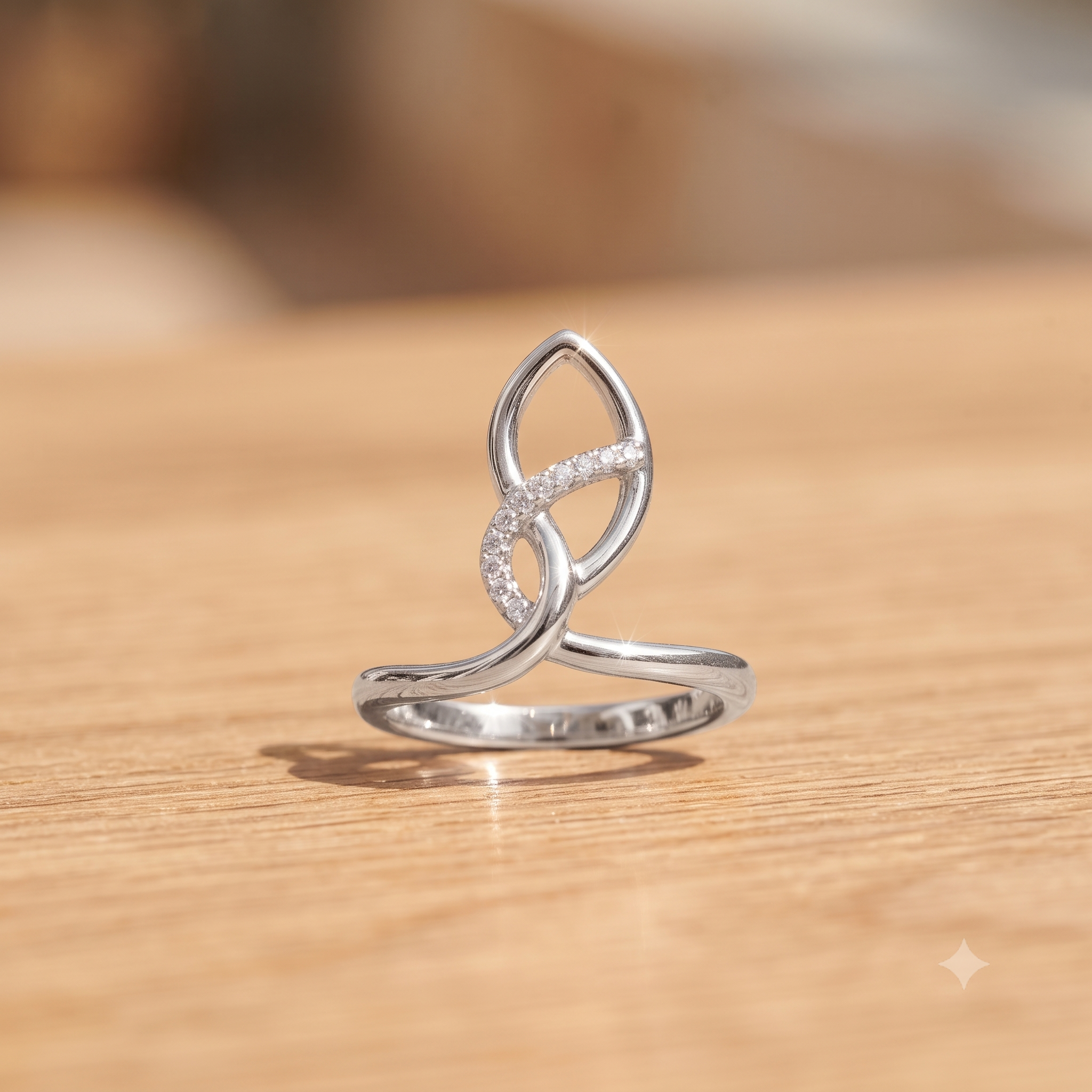 A silver open-band ring with a stylized infinity symbol set with small clear stones, resting on a light wood surface.