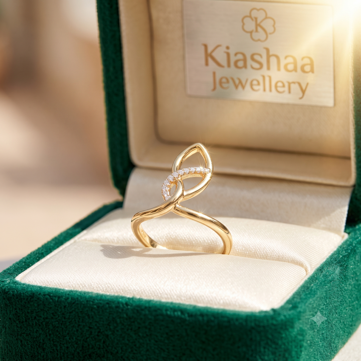 A gold ring with a small curved row of clear stones, displayed in an open green jewelry box. The inside lid shows the brand name 'Kiashaa Jewellery'.