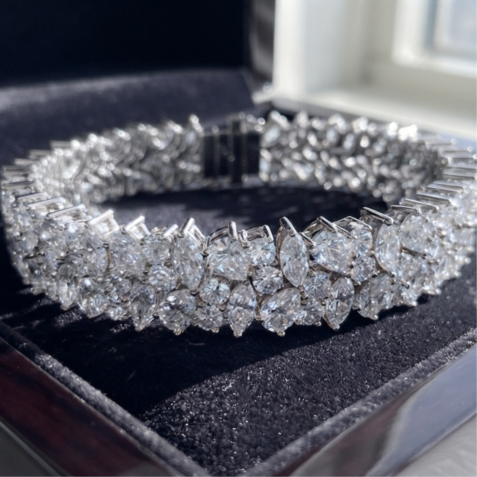 A diamond tennis bracelet with marquise and round,pear -cut stones in a silver-toned setting, displayed inside a black velvet jewelry box.