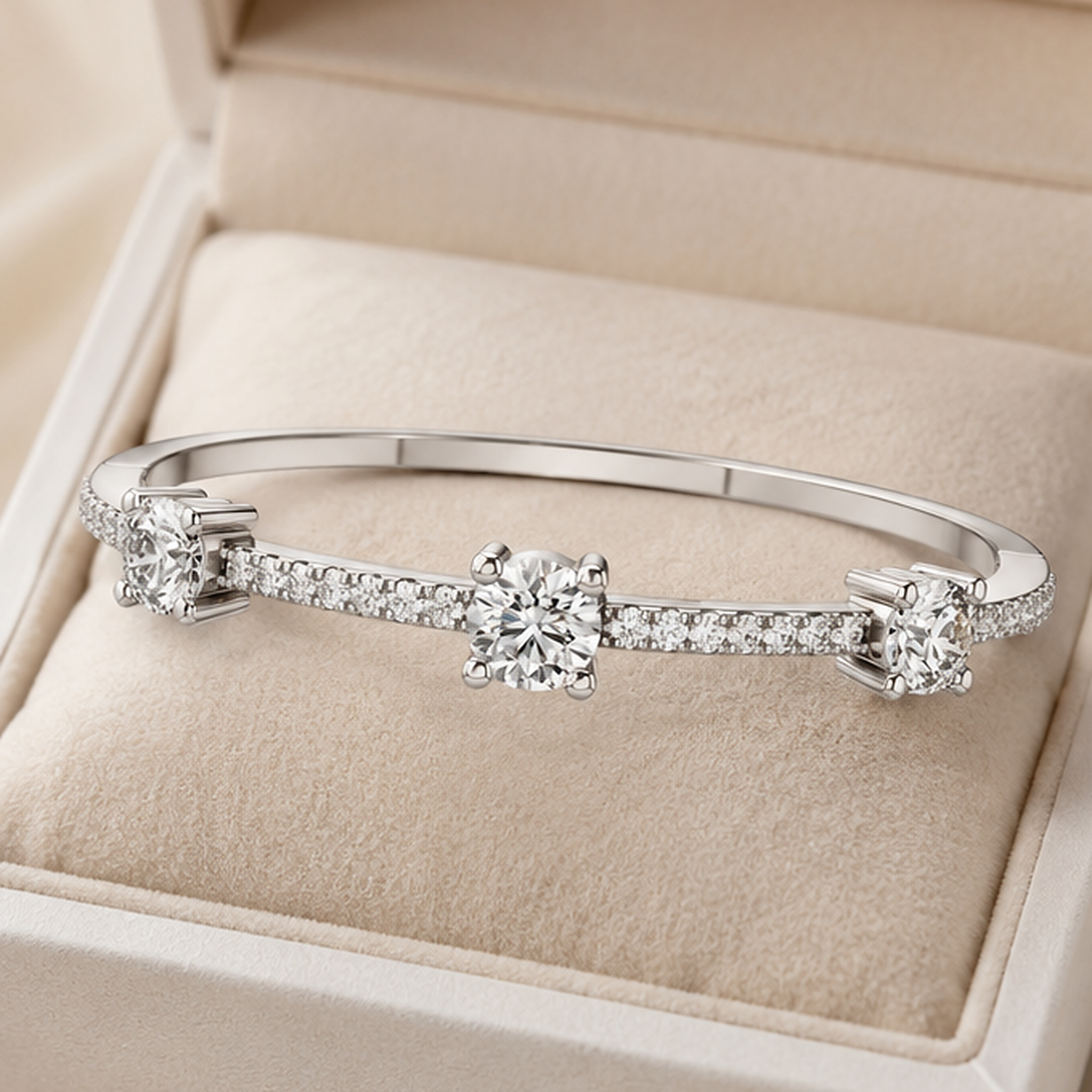 A silver-toned bangle bracelet with three round-cut center stones and small pavé accents, displayed on a beige jewelry box cushion.